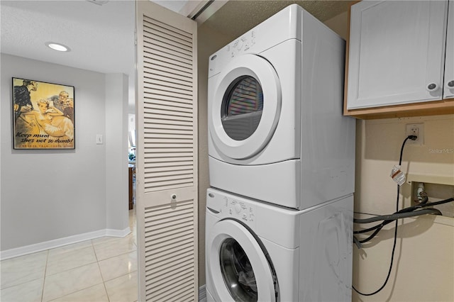 clothes washing area with stacked washer / drying machine, a textured ceiling, light tile patterned floors, and cabinets