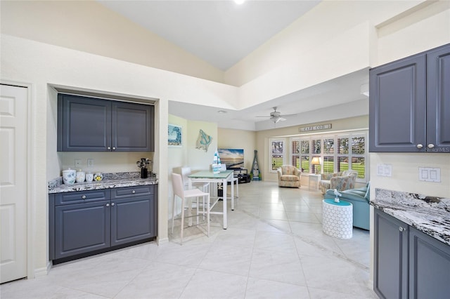 kitchen with lofted ceiling, light stone counters, and ceiling fan