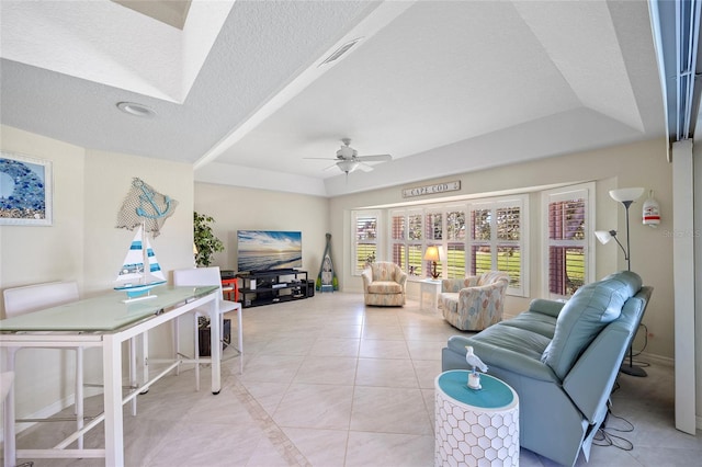 tiled living room featuring a tray ceiling, a textured ceiling, and ceiling fan