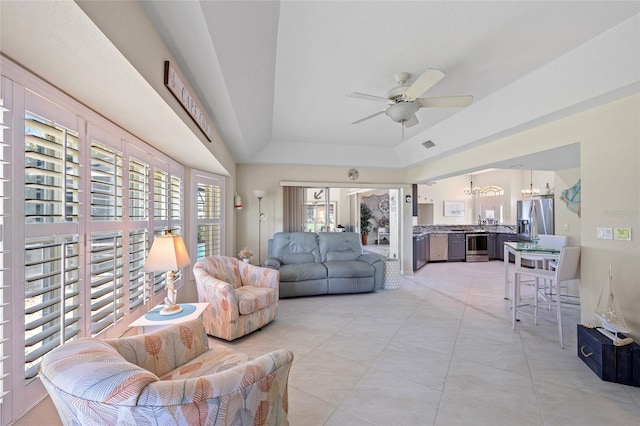 living room with a raised ceiling and ceiling fan with notable chandelier