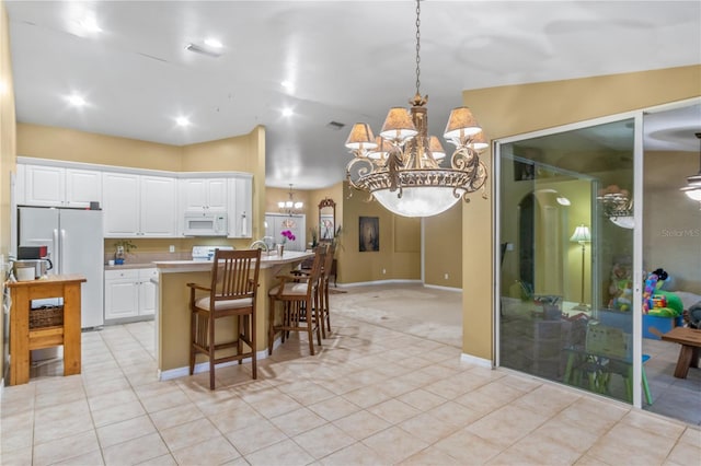 kitchen with white appliances, a center island, hanging light fixtures, a kitchen breakfast bar, and white cabinets