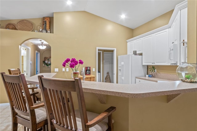 kitchen featuring a kitchen breakfast bar, kitchen peninsula, vaulted ceiling, white refrigerator with ice dispenser, and white cabinetry