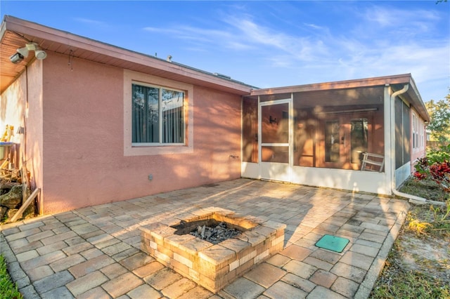 back of property with a sunroom, a patio area, and a fire pit