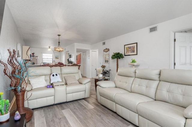 living room featuring a textured ceiling, an inviting chandelier, and light hardwood / wood-style flooring