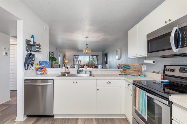 kitchen with sink, white cabinets, light hardwood / wood-style flooring, appliances with stainless steel finishes, and decorative light fixtures