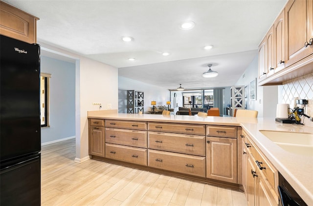 kitchen featuring sink, kitchen peninsula, black refrigerator, light wood-type flooring, and vaulted ceiling