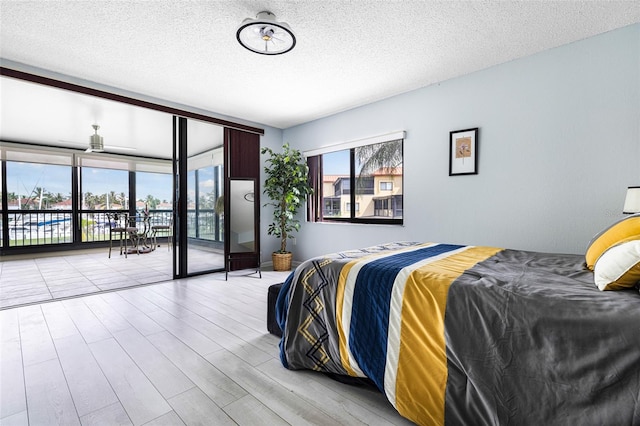 bedroom with a textured ceiling, light wood-type flooring, and access to exterior