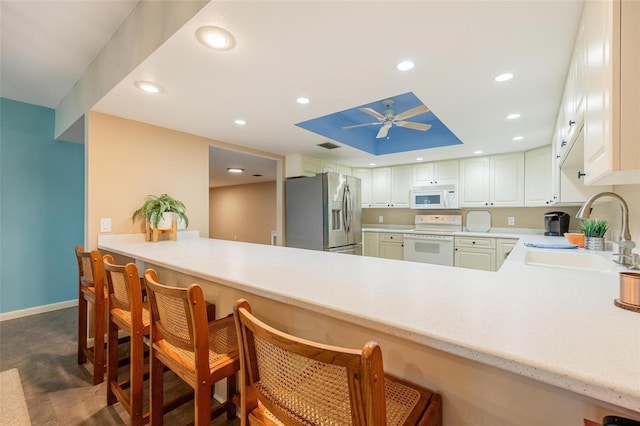 kitchen with kitchen peninsula, sink, white appliances, and a breakfast bar