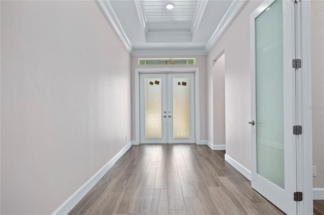 interior space with french doors, ornamental molding, light wood-type flooring, and a raised ceiling