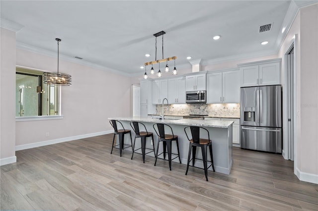 kitchen featuring light wood-type flooring, stainless steel appliances, pendant lighting, and a kitchen island with sink