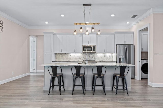 kitchen with washer / dryer, light stone countertops, appliances with stainless steel finishes, an island with sink, and white cabinets