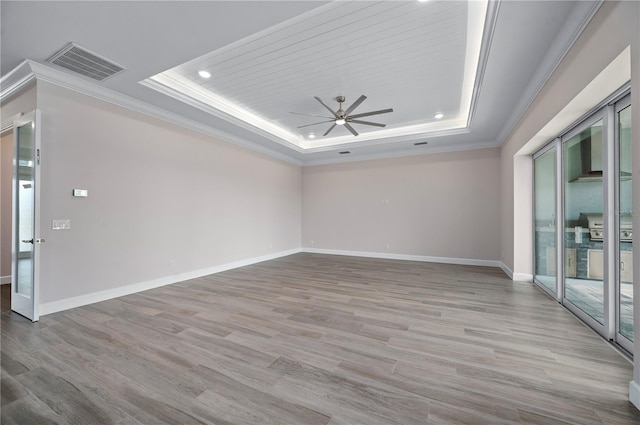 empty room with light hardwood / wood-style floors, a tray ceiling, and a wealth of natural light