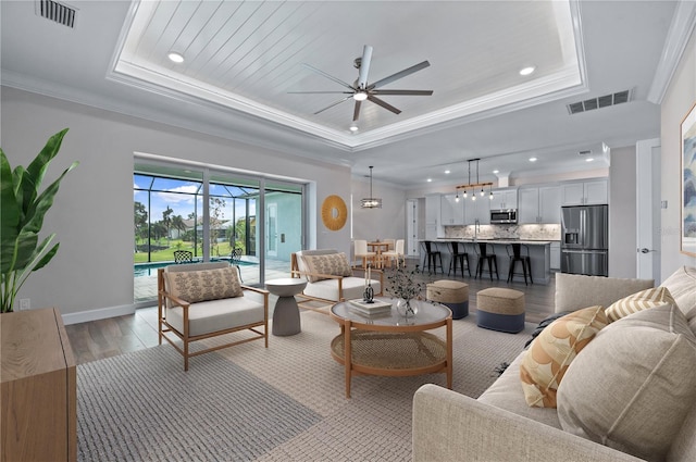 living room with light hardwood / wood-style floors, a raised ceiling, and ornamental molding