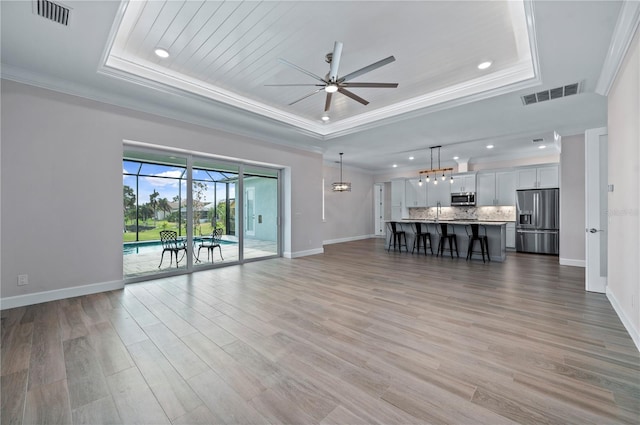 unfurnished living room featuring ornamental molding, wood-type flooring, a tray ceiling, and ceiling fan