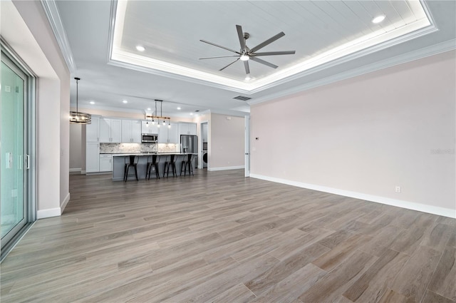 unfurnished living room with crown molding, light hardwood / wood-style flooring, a tray ceiling, and ceiling fan