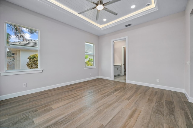 spare room with ceiling fan, wood-type flooring, a tray ceiling, and ornamental molding