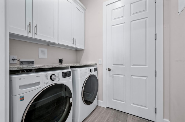 laundry area featuring cabinets, washing machine and dryer, and light hardwood / wood-style floors