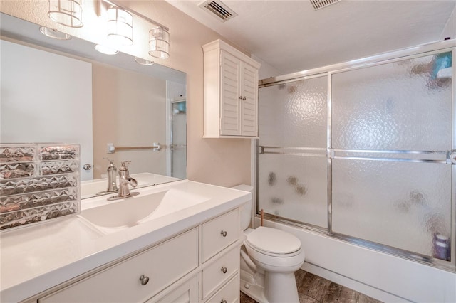 full bath featuring visible vents, toilet, wood finished floors, combined bath / shower with glass door, and vanity