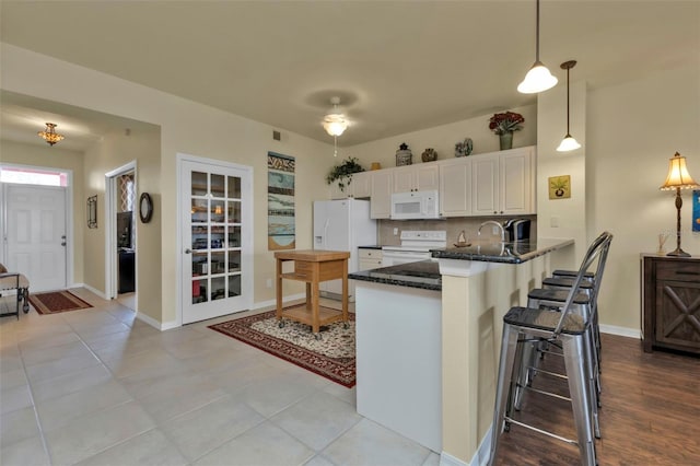 kitchen with pendant lighting, kitchen peninsula, white appliances, backsplash, and white cabinetry