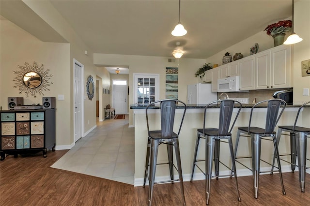 kitchen featuring light hardwood / wood-style floors, dark stone countertops, white cabinets, white appliances, and kitchen peninsula