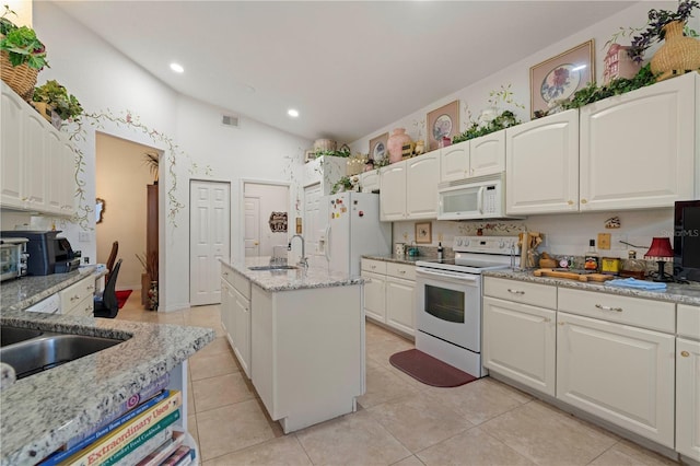 kitchen with white appliances, vaulted ceiling, light stone counters, and a kitchen island with sink