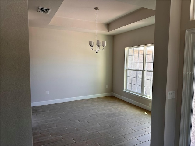 spare room featuring baseboards, visible vents, a raised ceiling, wood finished floors, and an inviting chandelier