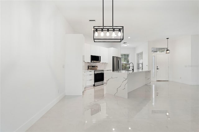 kitchen with a kitchen island with sink, stainless steel appliances, white cabinets, sink, and decorative light fixtures