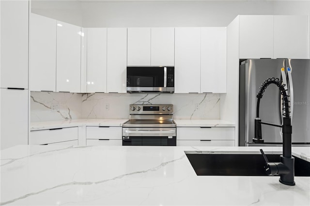 kitchen with white cabinets, appliances with stainless steel finishes, and light stone countertops