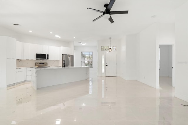 kitchen featuring a kitchen island with sink, pendant lighting, ceiling fan with notable chandelier, white cabinets, and appliances with stainless steel finishes