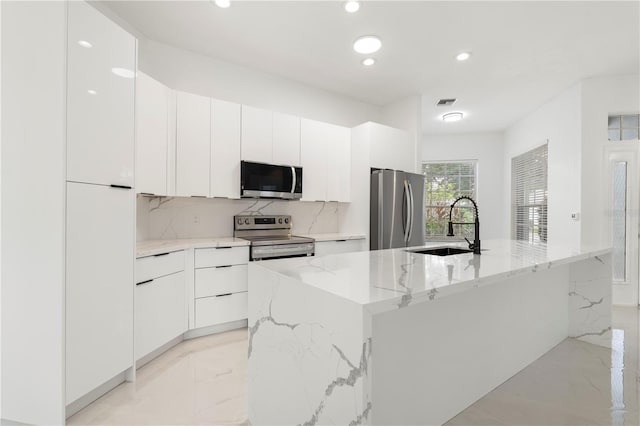 kitchen with white cabinets, appliances with stainless steel finishes, sink, and light stone countertops