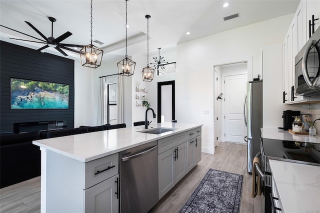 kitchen with light hardwood / wood-style floors, sink, an island with sink, appliances with stainless steel finishes, and light stone countertops