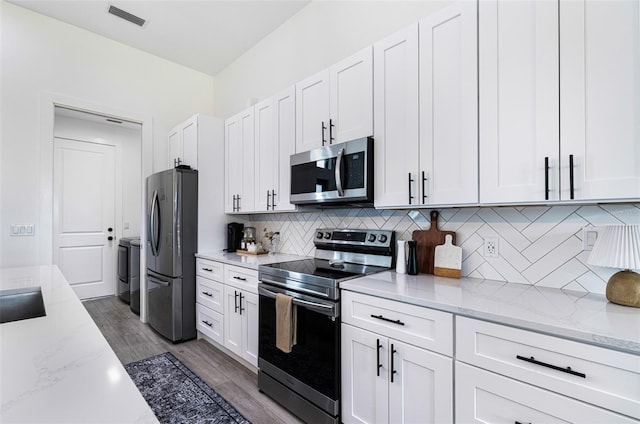 kitchen with light stone counters, dark wood-type flooring, white cabinets, decorative backsplash, and stainless steel appliances