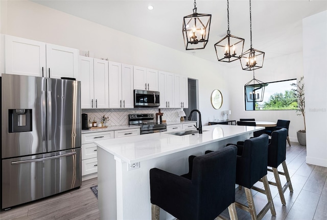 kitchen featuring an island with sink, white cabinetry, a kitchen breakfast bar, stainless steel appliances, and decorative light fixtures