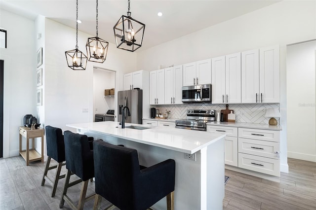 kitchen featuring pendant lighting, light hardwood / wood-style floors, a kitchen island with sink, a kitchen bar, and appliances with stainless steel finishes