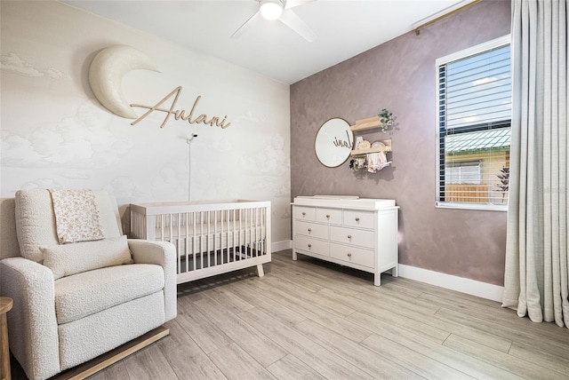 bedroom with light hardwood / wood-style floors, a crib, and ceiling fan