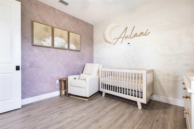 bedroom with ceiling fan, a nursery area, and light hardwood / wood-style floors