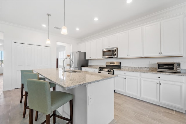 kitchen with appliances with stainless steel finishes, white cabinetry, hanging light fixtures, and an island with sink