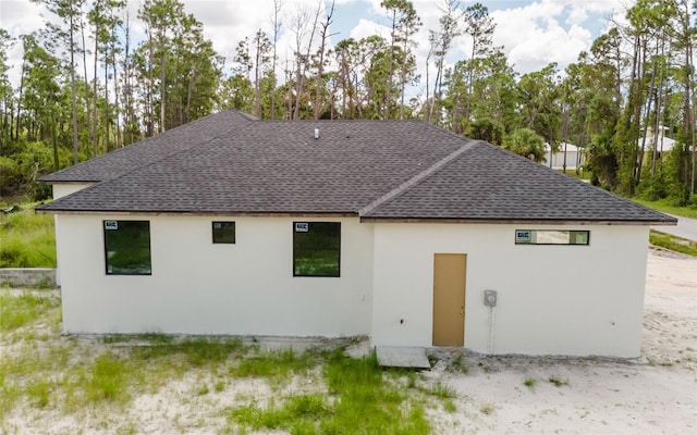 2502 Pinewood St, North Port, FL 34288 - back of property featuring a shingled roof, stucco siding, and view of wooded area