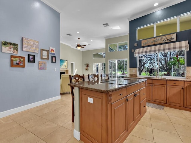 kitchen featuring dark stone counters, black electric stovetop, a kitchen island, crown molding, and ceiling fan