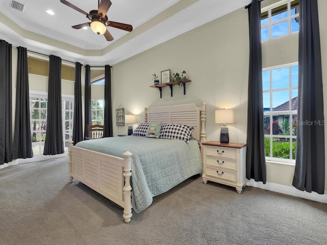 carpeted bedroom featuring ceiling fan, a raised ceiling, and multiple windows