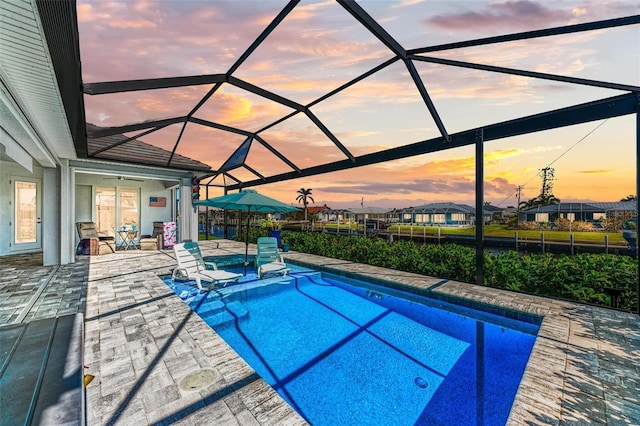 pool at dusk featuring a patio and a lanai