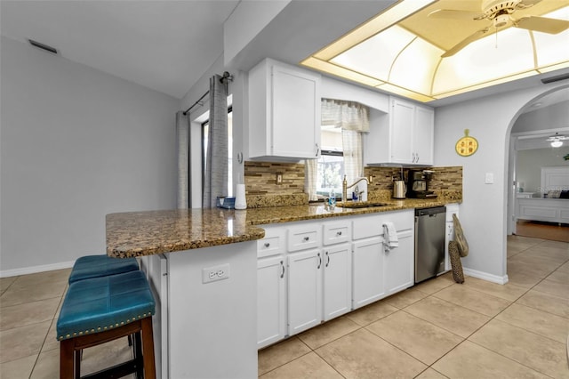 kitchen featuring dark stone countertops, dishwasher, kitchen peninsula, and white cabinetry