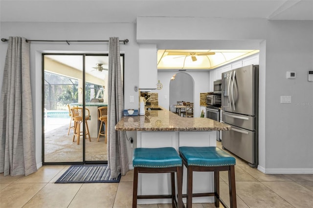 kitchen with a breakfast bar, light stone counters, white cabinets, kitchen peninsula, and appliances with stainless steel finishes