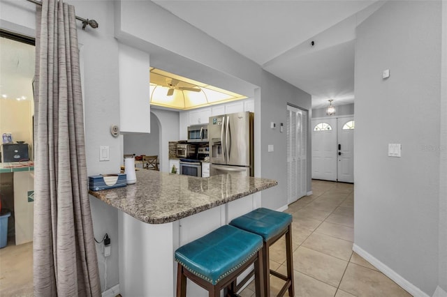 kitchen with dark stone countertops, a breakfast bar, kitchen peninsula, light tile patterned floors, and stainless steel appliances