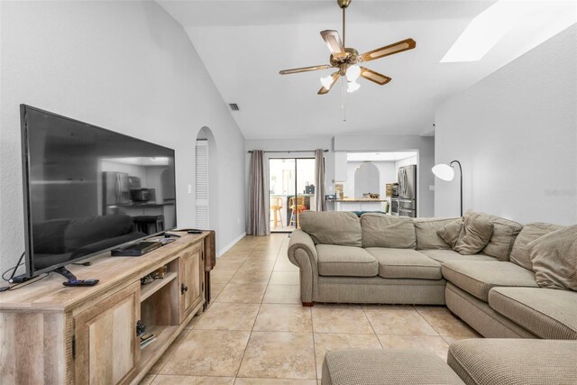 tiled living room featuring high vaulted ceiling, ceiling fan, and a skylight