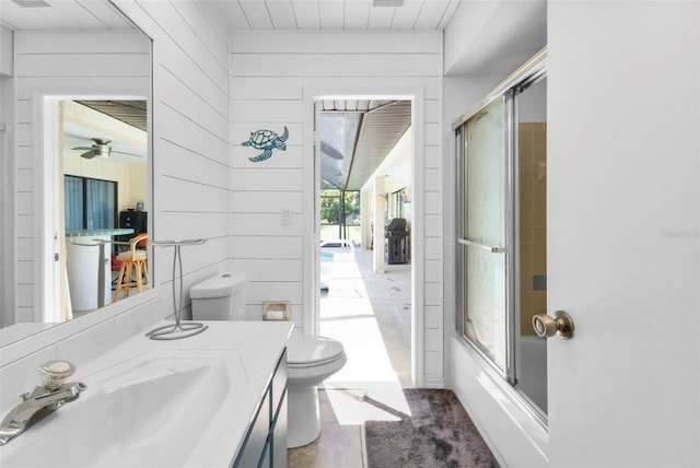 full bathroom with wood walls, shower / bath combination with glass door, vanity, and toilet