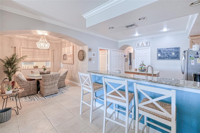 kitchen with light stone countertops, stainless steel refrigerator, crown molding, an inviting chandelier, and a textured ceiling