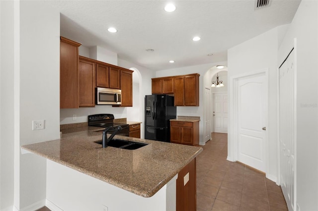 kitchen featuring arched walkways, a peninsula, a sink, brown cabinets, and black appliances