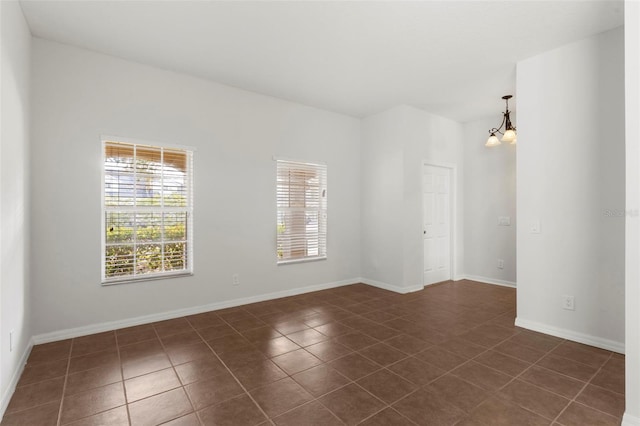 empty room featuring baseboards, dark tile patterned flooring, and an inviting chandelier