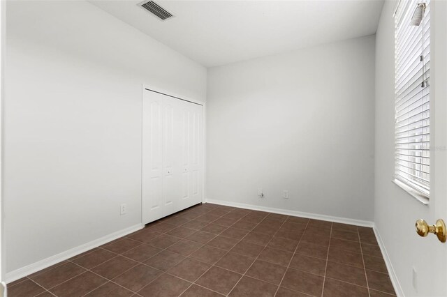 unfurnished bedroom featuring dark tile patterned flooring, a closet, visible vents, and baseboards